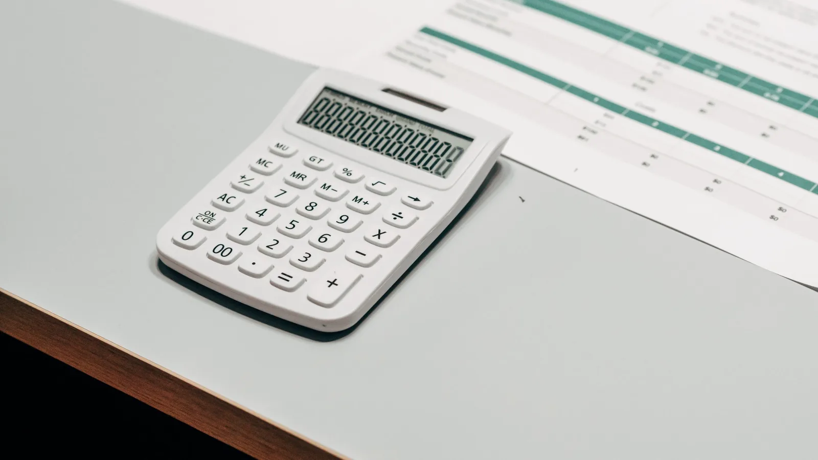 A calculator resting on a printed spreadsheet on a white desk
