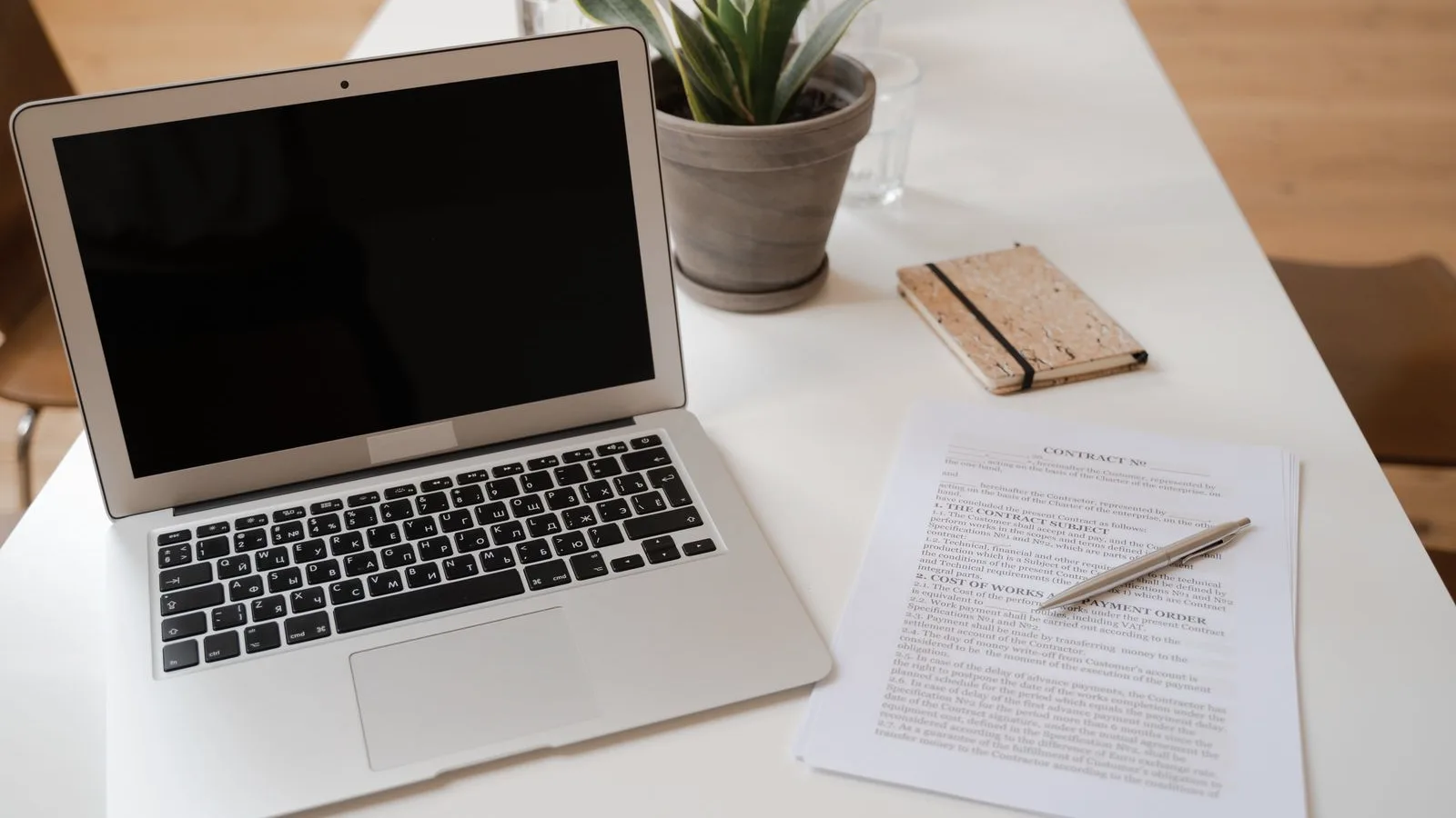 A laptop, potted plant, and printed documents arranged on a desk