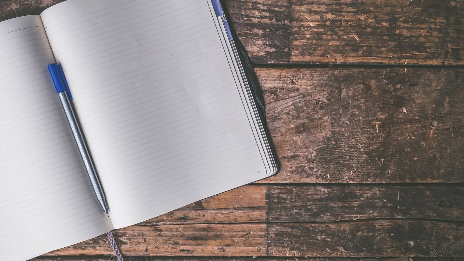 An open blank notebook and a pen on a wooden table