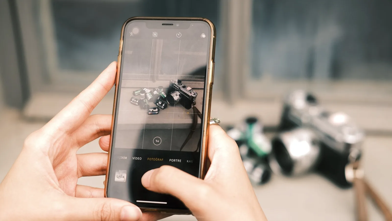 Someone holding a phone to photograph a vintage camera and rolls of film on a table